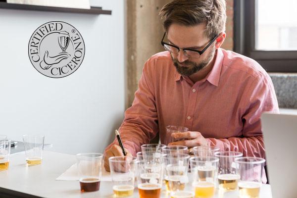 A person involved in a beer tasting exam. There are many tasting cups full of different beers in front of them. A Certified Cicerone logo is in the background.